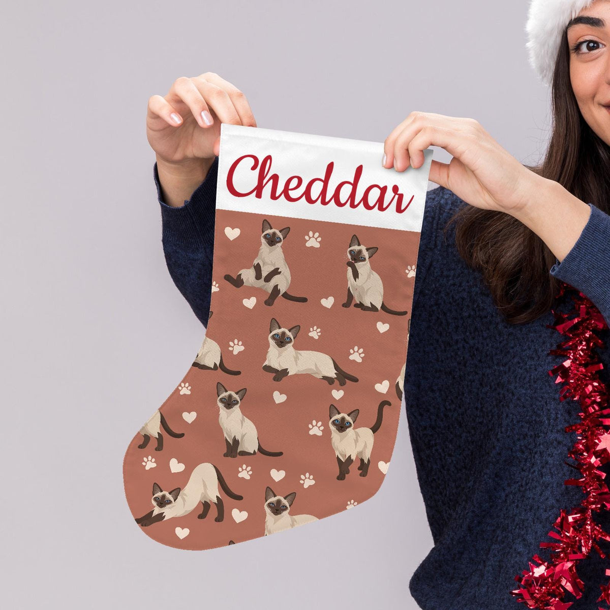 Siamese Christmas stocking on muted terracotta background with example name Cheddar in red script on the white cuff; view 5.