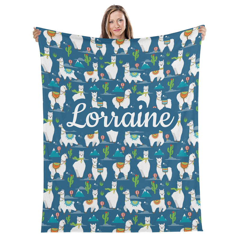 A woman holding a blue blanket with a repeating pattern of white llamas and various colorful elements such as mountains, cacti, and hot air balloons.