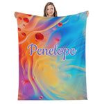 A woman is holding up a colorful, abstract printed blanket with the name "Penelope" written on it.