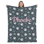 A woman is holding up a blanket with a repeating pattern of panda faces and leaves in shades of green and gray.