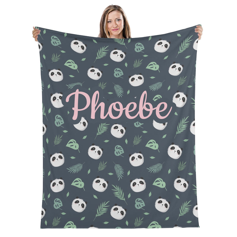 A woman is holding up a blanket with a repeating pattern of panda faces and leaves in shades of green and gray.