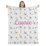 A woman holding up a white blanket with a repeating pattern of llamas and cacti.