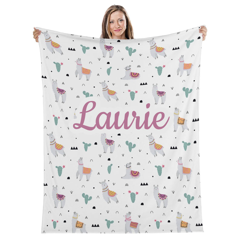 A woman holding up a white blanket with a repeating pattern of llamas and cacti.