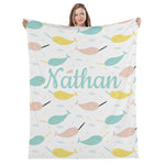 A woman is holding up a white blanket with a repeating pattern of colorful narwhals and stars.