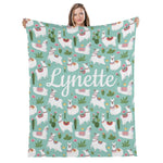 A woman holding a blanket with a repeating pattern of llamas, cacti, and other colorful elements.
