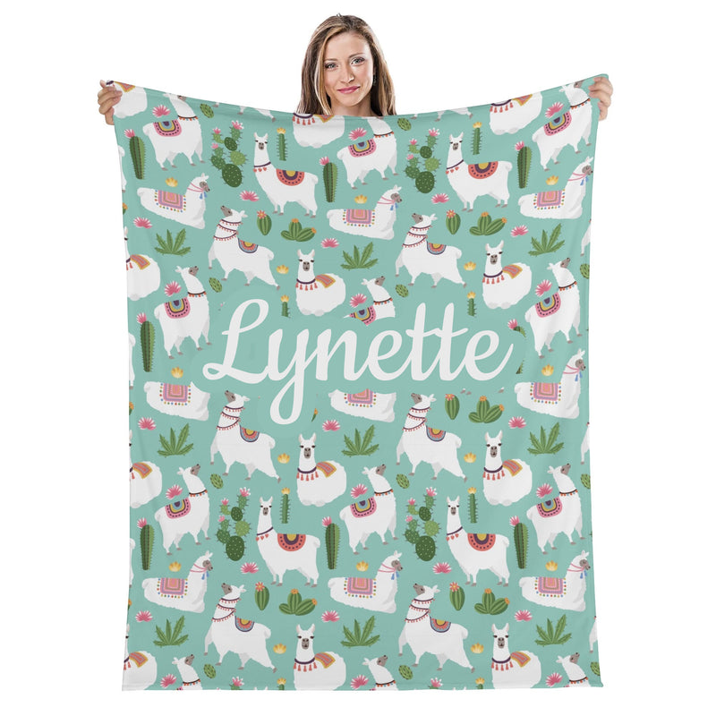 A woman holding a blanket with a repeating pattern of llamas, cacti, and other colorful elements.