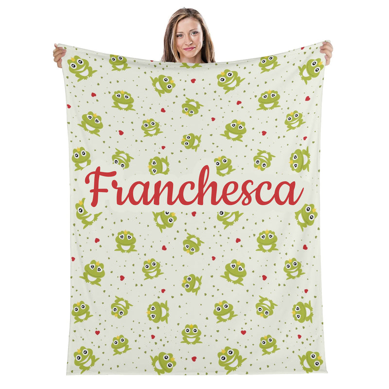 A woman is holding up a blanket with a repeating pattern of green frogs and red hearts.