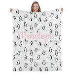 A woman is holding up a blanket with a repeating pattern of penguins and snowflakes.