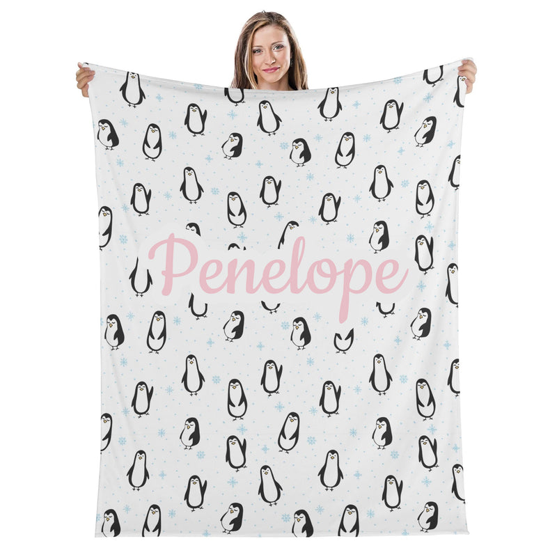 A woman is holding up a blanket with a repeating pattern of penguins and snowflakes.