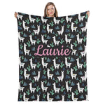 A woman is holding up a black blanket with a repeating pattern of white llamas and cacti on a black background.
