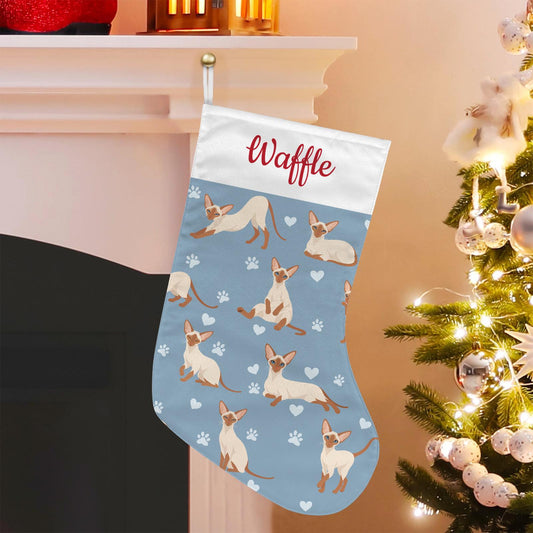 Colorpoint Shorthair Christmas stocking on dusty blue background with example name Waffle in red script on the white cuff; view 1.
