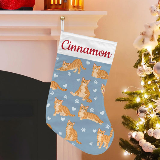 Domestic Shorthair Orange Christmas stocking on dusty blue background with example name Cinnamon in red script on the white cuff; view 1.