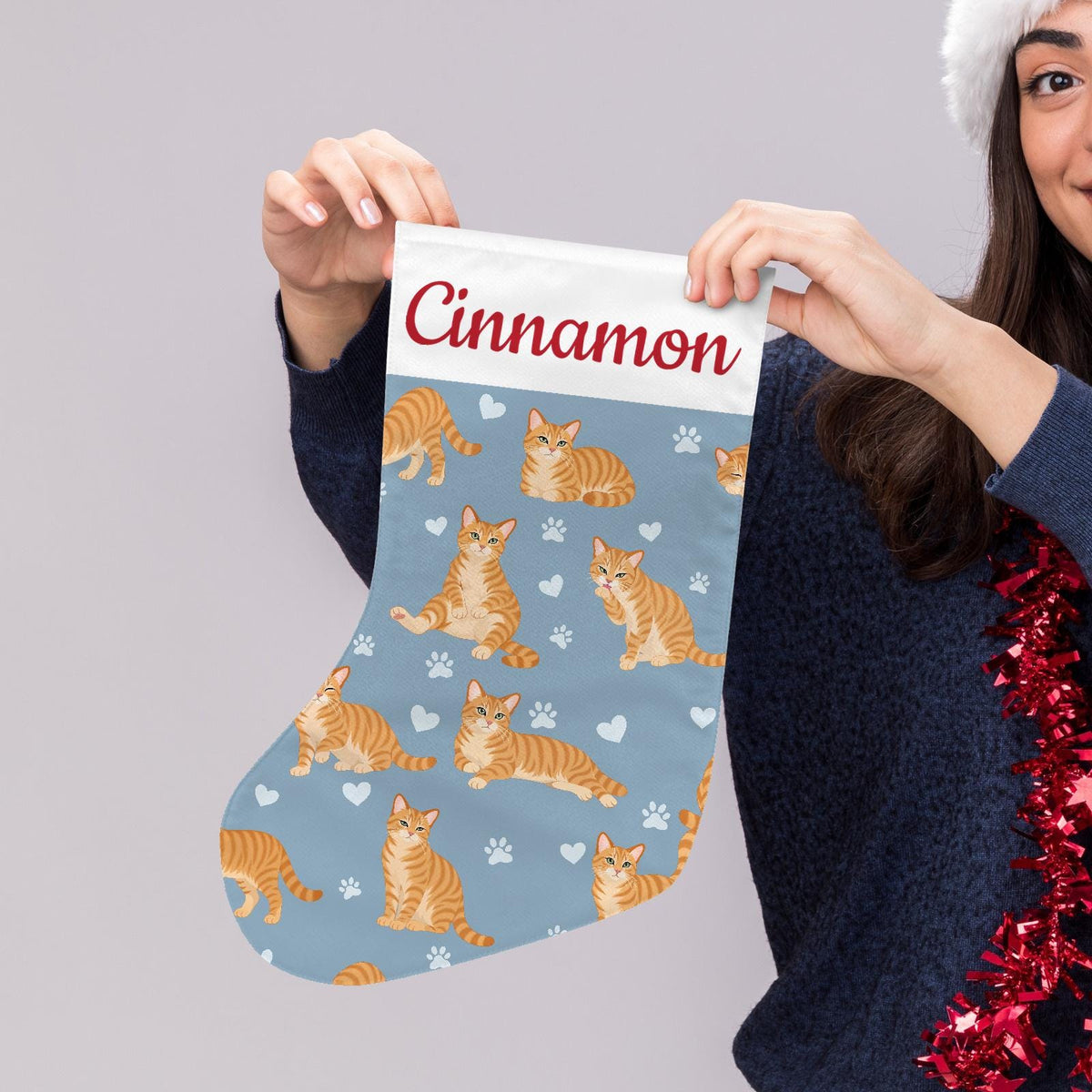 Domestic Shorthair Orange Christmas stocking on dusty blue background with example name Cinnamon in red script on the white cuff; view 5.