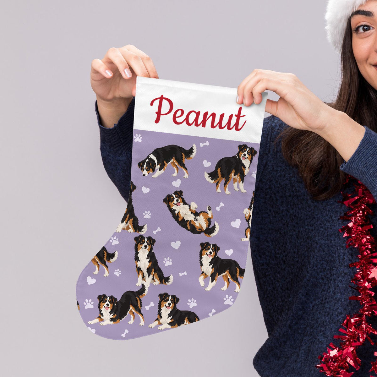 Miniature American Shepherd Christmas stocking on soft lavender background with example name Peanut in red script on the white cuff; view 5.