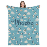 A woman is holding up a blue blanket with a repeating pattern of penguins and ice formations.