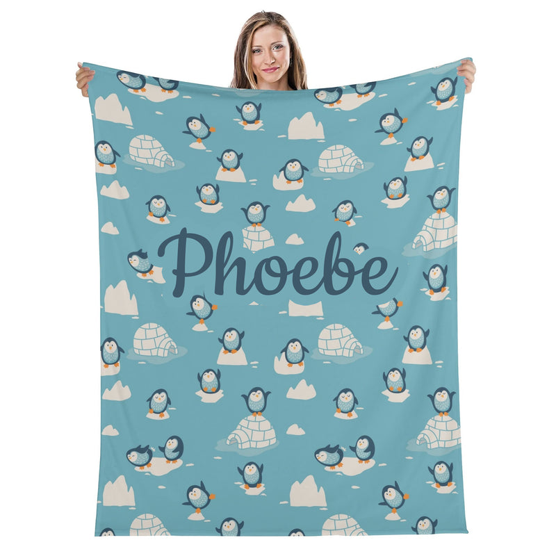 A woman is holding up a blue blanket with a repeating pattern of penguins and ice formations.