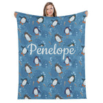 A woman is holding up a blue blanket with a repeating pattern of penguins and bubbles.