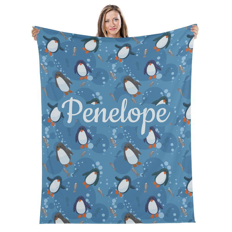 A woman is holding up a blue blanket with a repeating pattern of penguins and bubbles.