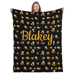 A woman is holding up a black blanket with a repeating pattern of yellow bees and white flowers.
