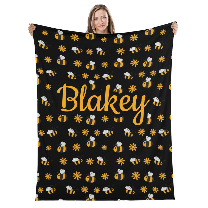 A woman is holding up a black blanket with a repeating pattern of yellow bees and white flowers.
