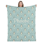 A woman is holding up a light blue blanket with a repeating pattern of penguins and triangles.