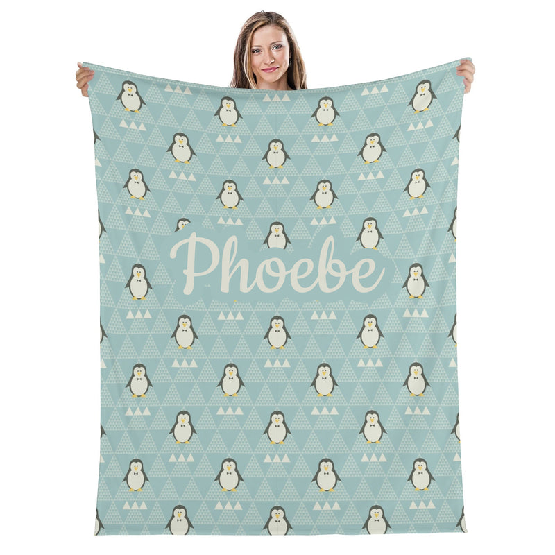 A woman is holding up a light blue blanket with a repeating pattern of penguins and triangles.