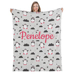 A woman is holding up a gray blanket with a repeating pattern of penguins and clouds.