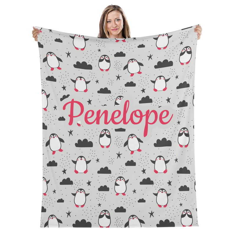 A woman is holding up a gray blanket with a repeating pattern of penguins and clouds.