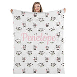 A woman is holding up a white blanket with a repeating pattern of panda bears and the name "Penelope" printed on it.