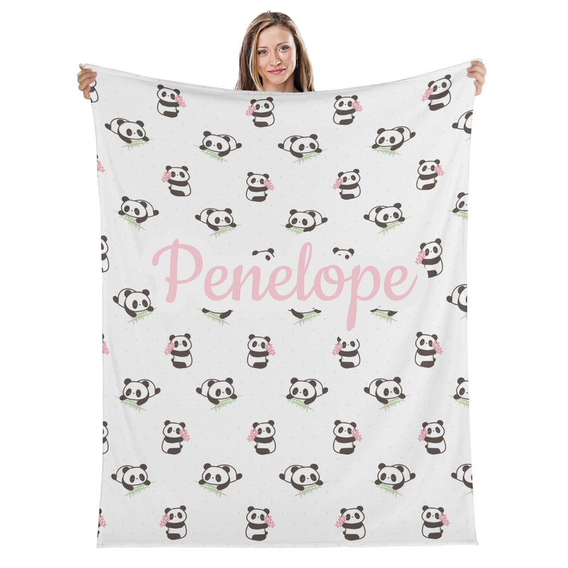 A woman is holding up a white blanket with a repeating pattern of panda bears and the name "Penelope" printed on it.