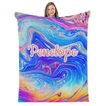 A woman is holding up a colorful, abstract, and swirling blanket with the name "Penelope" printed on it.