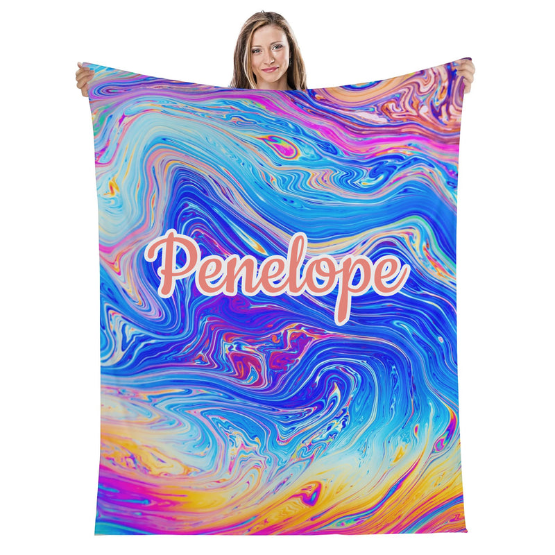 A woman is holding up a colorful, abstract, and swirling blanket with the name "Penelope" printed on it.