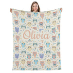 A woman is holding up a blanket with a repeating pattern of colorful owls and the name "Olivia" written on it.