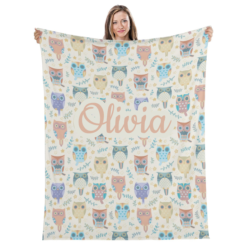 A woman is holding up a blanket with a repeating pattern of colorful owls and the name "Olivia" written on it.